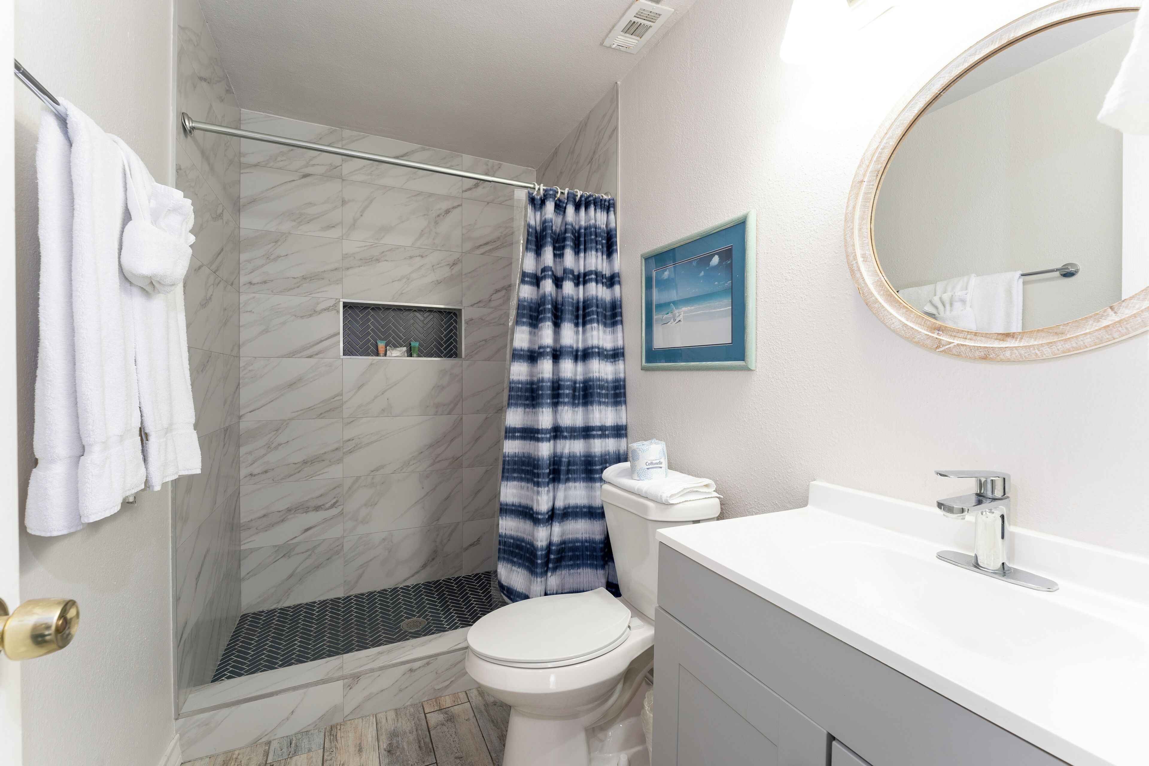 A bathroom with a shower, toilet, sink, and a mirror.