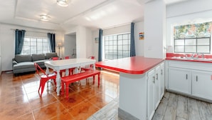 Una cocina moderna con armarios blancos, encimera roja y un comedor con mesa blanca y sillas rojas.