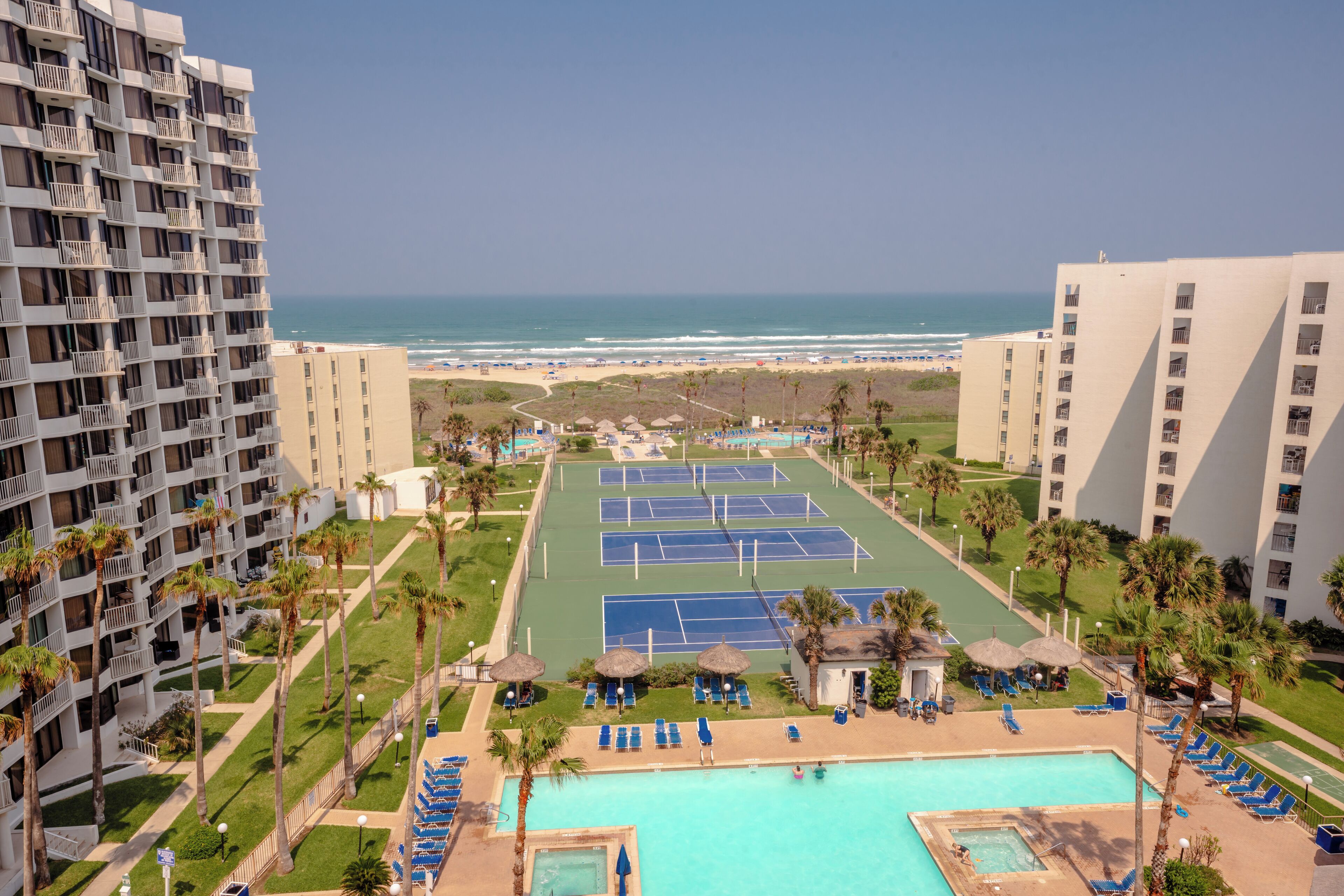 A hotel with a pool area, tennis courts, and a view of the beach.