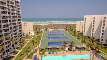 A hotel with a pool area, tennis courts, and a view of the beach.