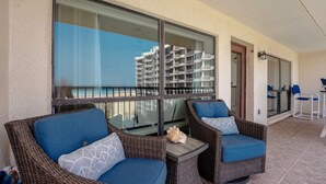 A balcony with wicker furniture, a glass table, and a view of a high-rise building.