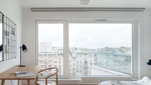 Une chambre avec une grande fenêtre, un lit, un bureau et une chaise.