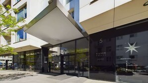 Une entrée d’hôtel moderne avec une façade en verre, un logo en forme d’étoile et une enseigne indiquant « Silver House Invest ».