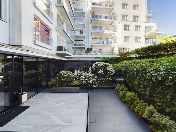 A modern building with multiple balconies and a landscaped courtyard with hedges and flowering plants.