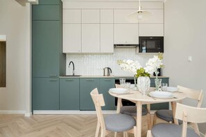 A modern kitchen with teal cabinets, a white countertop, and a dining area with a round table and chairs.