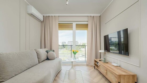 A modern living room with a sofa, a coffee table, a TV, and a balcony with a view.