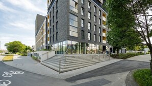 A modern building with a staircase leading to the entrance, a bike lane, and a clear sky.