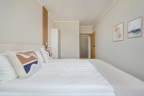 A hotel room with a large bed, a wardrobe, a door leading to a bathroom, and two framed artworks on the wall. - Modern Apartment | Parking, Gym and Air Conditioning (Wrocław)