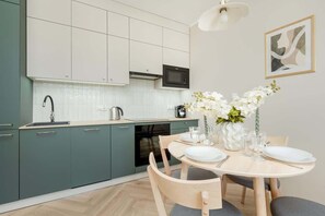 A modern kitchen with teal cabinets, a microwave, and a dining area with a table set for two. - Modern Apartment | Parking, Gym and Air Conditioning (Wrocław)