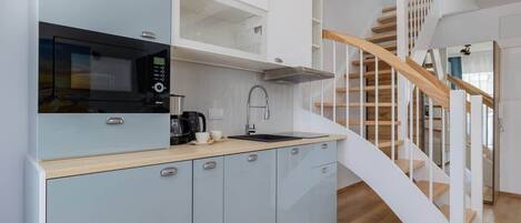 A modern kitchen with light blue cabinets, a black microwave, and a wooden staircase.