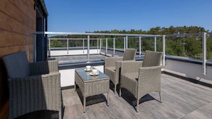 A rooftop terrace with wicker furniture, a table with cups, and a clear view of the surrounding landscape.