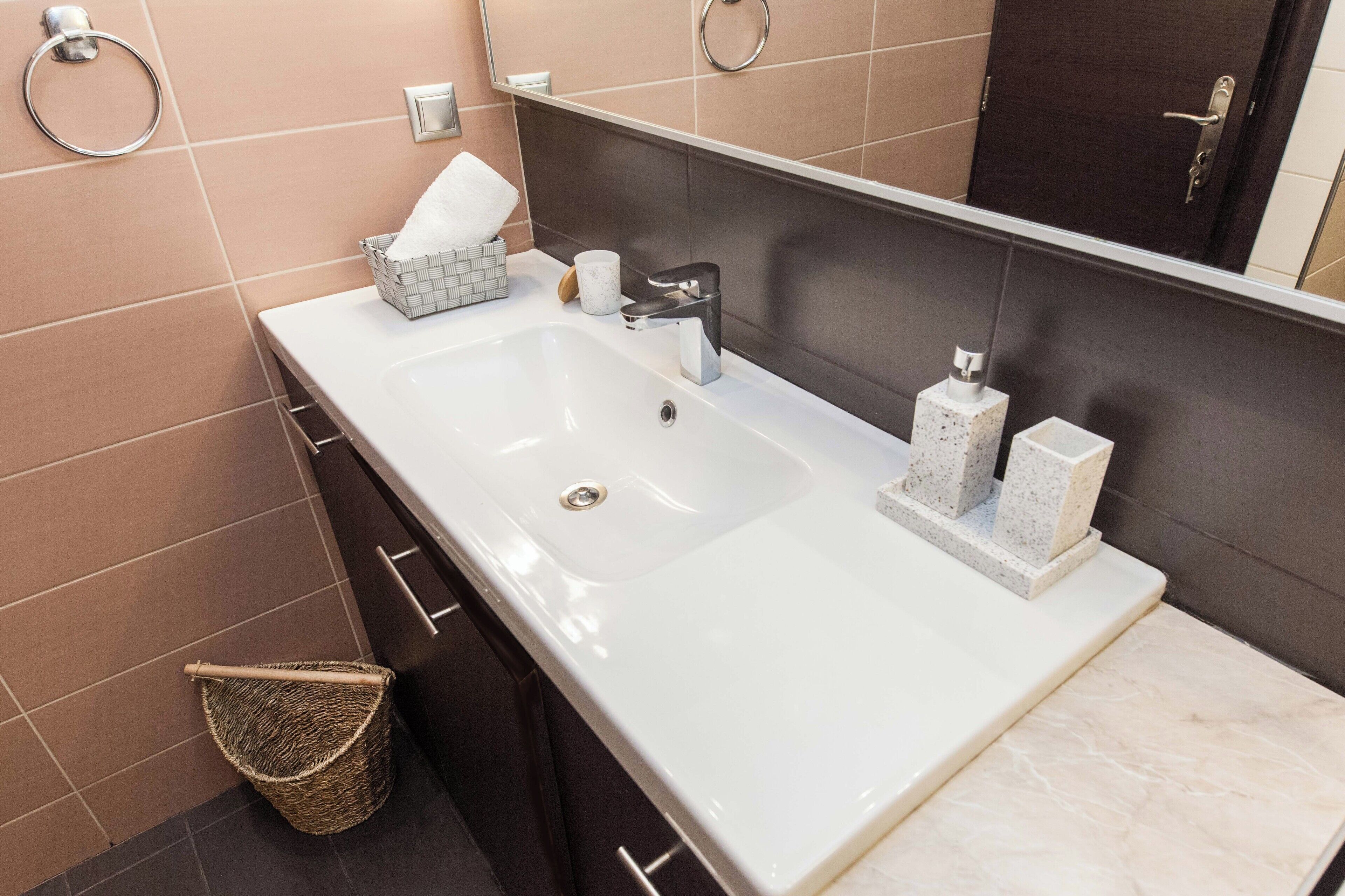 A modern bathroom with a white sink, dark tiles, a mirror, and a towel rack.