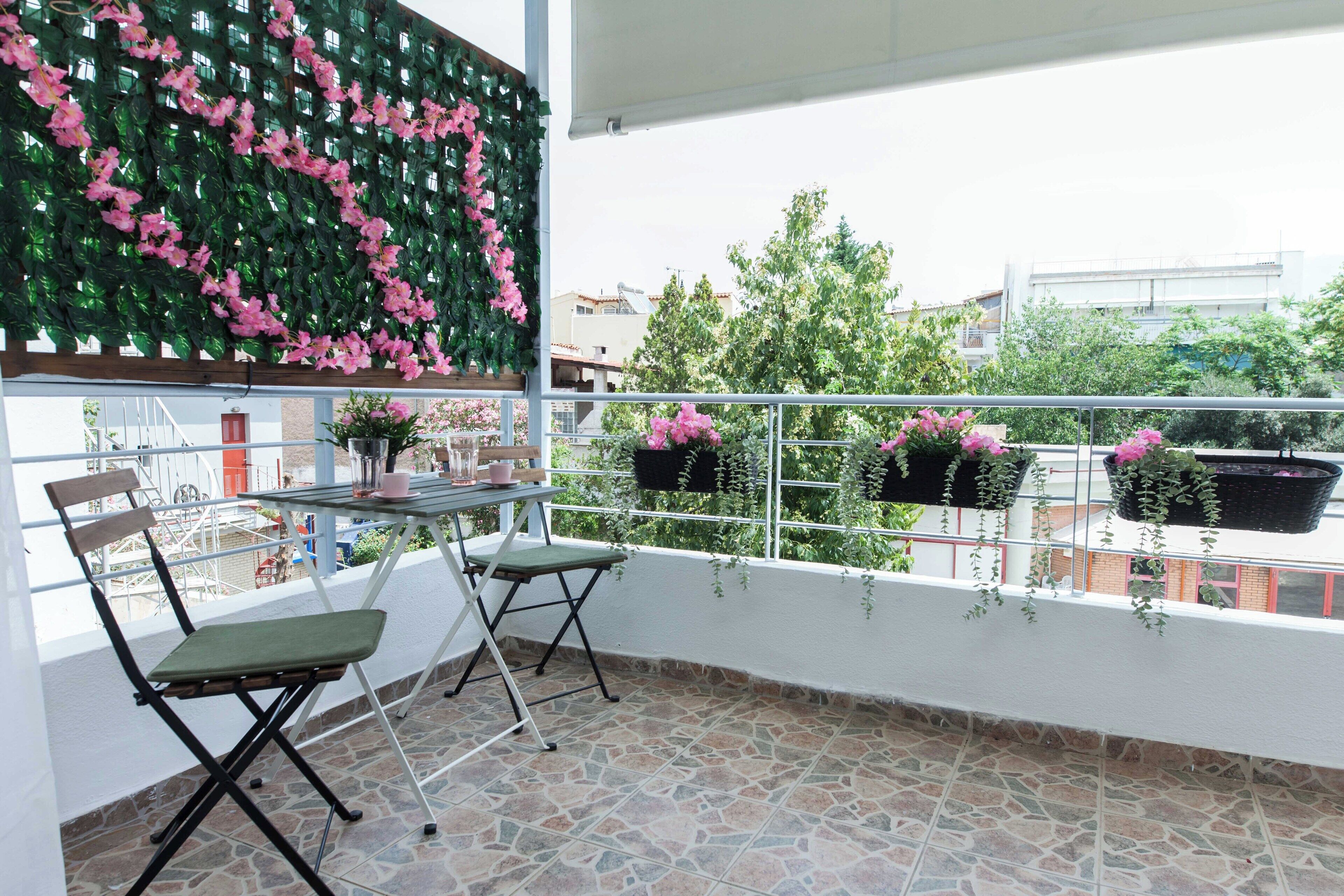 A balcony with a table and chairs, potted plants, and a view of buildings and trees.