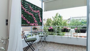 En balkong med ett bord och stolar, en grön vägg med rosa blommor och hängande blomkrukor med rosa blommor.