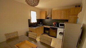 A compact kitchen with wooden cabinets, a microwave, a dishwasher, and a dining area with a table and chairs. - Family-friendly, Cozy and Peaceful Villa with Pool in Apt en Luberon, Provence (Apt)