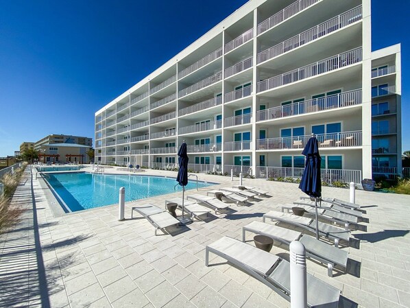 Um hotel moderno com área de piscina, várias varandas e espreguiçadeiras.