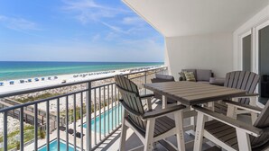 Ein Balkon mit Blick auf Strand und Meer, ein Pool und Gartenmöbel.