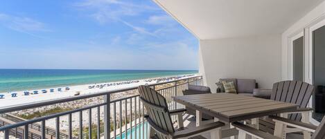 A balcony with a view of the beach and ocean, a pool, and outdoor furniture.