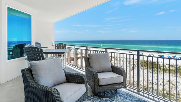 Ein Balkon mit Rattanmöbeln, einem Glastisch und Blick auf Strand und Meer.