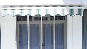 A building with a white exterior, a large glass door with a metal handle, and a green and white striped awning above the door. - A Casa di Doralucia - Santa Maria di Leuca (Santa Maria di Leuca)