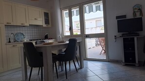 A compact kitchen with a dining area, a TV on a stand, and a view of the outside through the door. - A Casa di Doralucia - Santa Maria di Leuca (Santa Maria di Leuca)