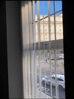 Vista a través de persianas de un edificio con numerosas ventanas y un estacionamiento lleno de coches.