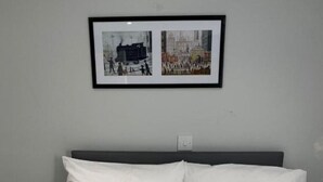 A neatly made bed with white linens and a single silver pillow, set against a grey wall with two framed pictures above it. - Brownlows Inn Rooms  (Liverpool)