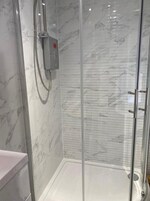 Un baño moderno con cabina de ducha de vidrio, paredes de mármol y panel de control.