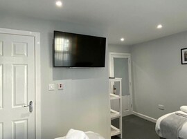 Una habitación de hotel con una cama, un televisor montado en la pared, un armario blanco y una puerta.