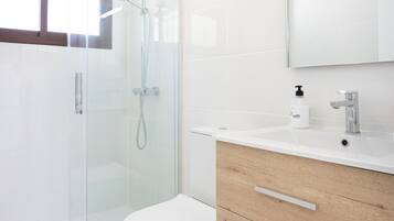 Un baño moderno con ducha envuelta en vidrio, inodoro blanco y tocador de madera con espejo.