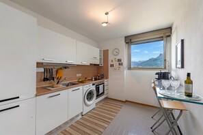 Eine moderne Küche mit Waschmaschine, einem Essbereich mit Tisch und Stühlen sowie einem Fenster mit Blick auf die Berge.