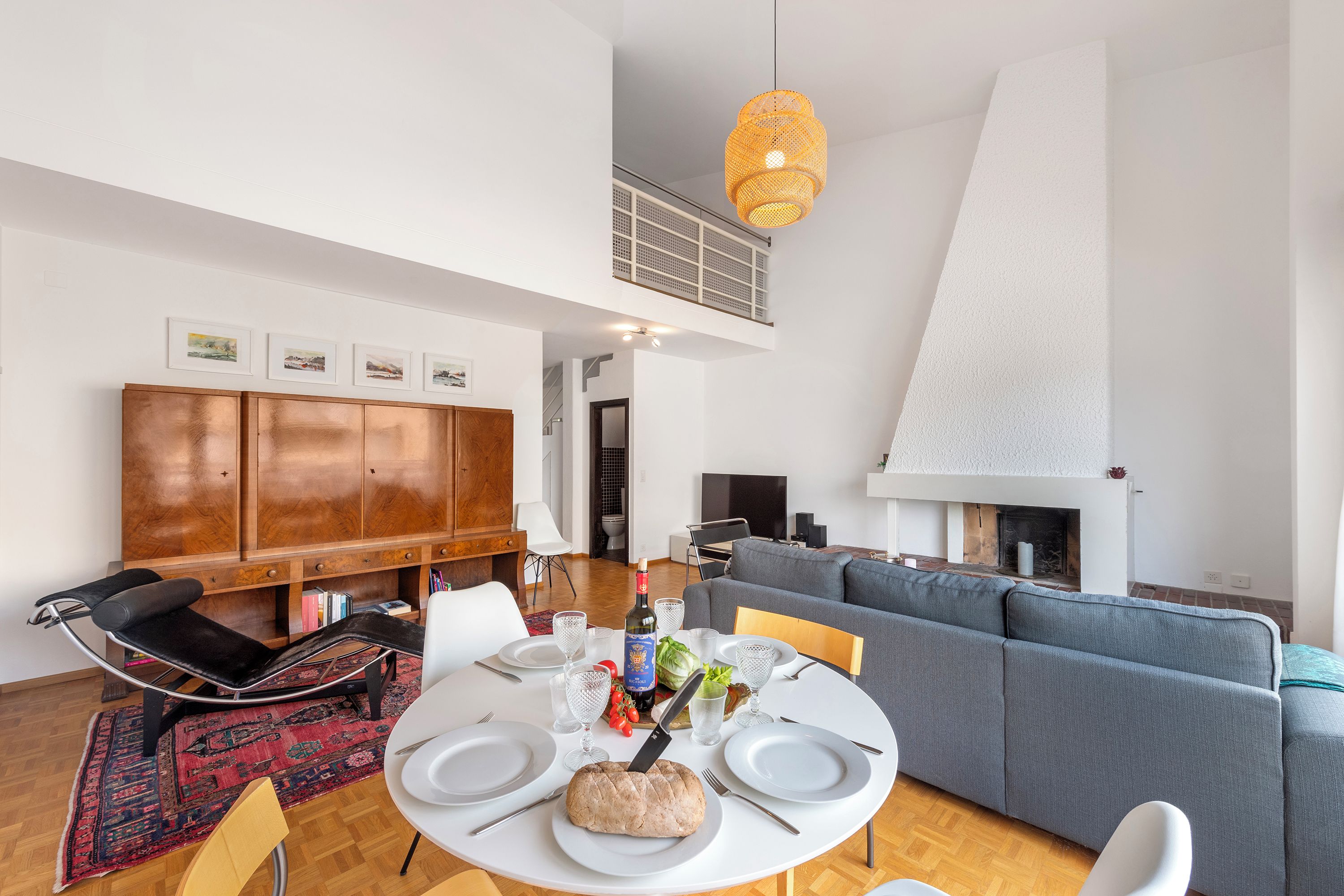 A modern living room with a dining area, a fireplace, and a high ceiling.