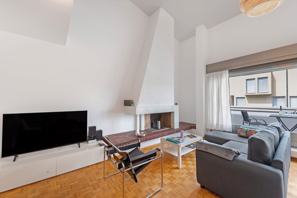 Una sala de estar moderna con una televisión de pantalla plana, chimenea, sofá y comedor con mesa y sillas.