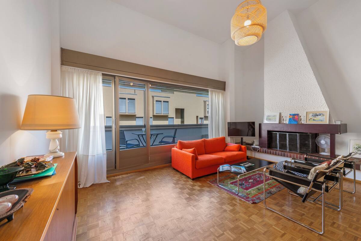 Una sala de estar moderna con un sofá, una mesita de centro, una chimenea y un ventanal con cortinas.