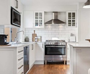 A modern kitchen with white cabinetry, a stainless steel range hood, and a built-in oven. - Stunning Family Home on Prince - Close to CBD! (Orange)