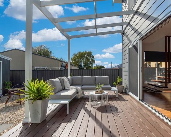 Une terrasse extérieure couverte, aménagée avec un canap é, une table basse et des plantes en pot.