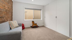 A room with a grey sofa, a rocking horse, a window, and a white wardrobe. - Stunning Family Home on Prince - Close to CBD! (Orange)