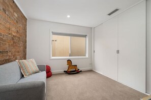Une pièce avec un canapé gris, un cheval à bascule, une fenêtre et une armoire blanche.