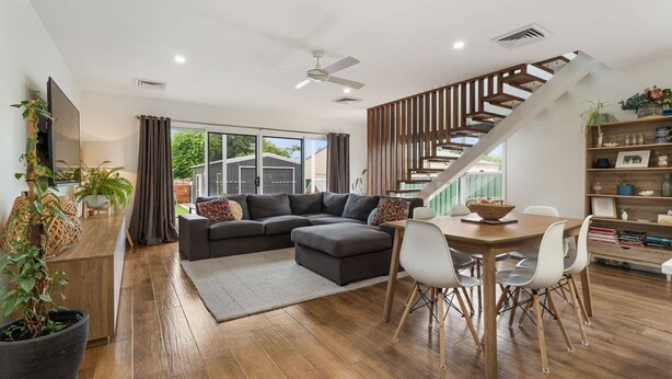 A modern living room with a sectional sofa, a dining table with chairs, a staircase, and a bookshelf. - Stunning Family Home on Prince - Close to CBD! (Orange)