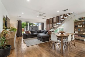A modern living room with a sectional sofa, a dining table with chairs, a staircase, and a bookshelf. - Stunning Family Home on Prince - Close to CBD! (Orange)