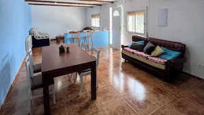 A spacious living area with a wooden dining table, a sofa, and a kitchen area in the background.