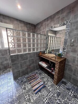 Un baño con piso de baldosas, tocador de madera, espejo y ventana.