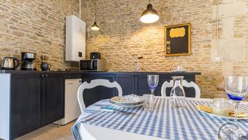 A kitchen with a stone wall, a dining table with a blue and white checkered tablecloth, and a hanging light fixture.