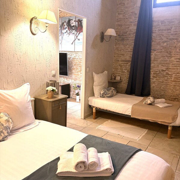 A hotel room with two beds, a small desk, a wall-mounted TV, and a decorative painting.