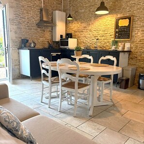 Una cocina con pared de piedra, una mesa de comedor con sillas blancas y una cafetera.