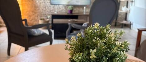 Un salon avec une table ronde, un panier en osier contenant des plantes vertes, un téléviseur et un mur en pierre.