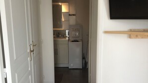 A narrow hallway leading to a kitchen with white cabinets, a refrigerator, and a wooden floor. - Joli Appartement T2 Vannes / 2 à 4 Personnes (Vannes)