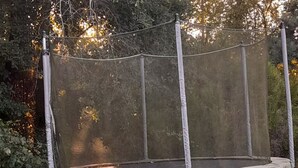A trampoline with a safety net, set on a grassy lawn.