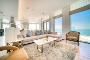 A modern living room with a sofa, armchair, coffee table, and large windows overlooking the ocean.