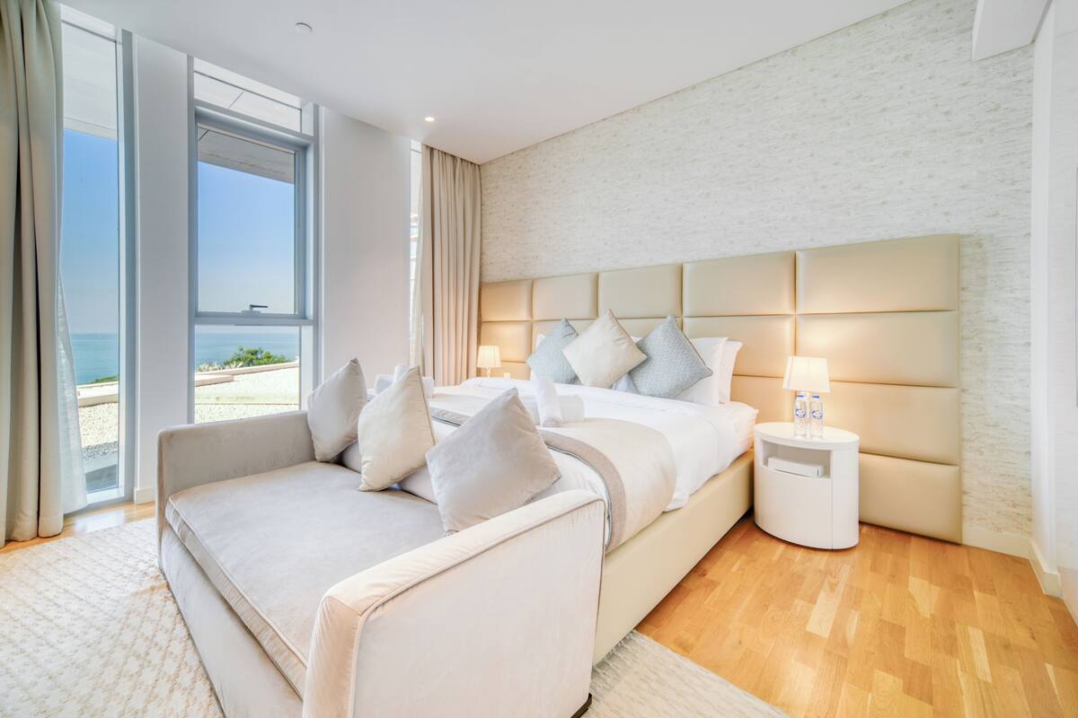 A modern bedroom with a large bed, a sofa, and a view of the sea.